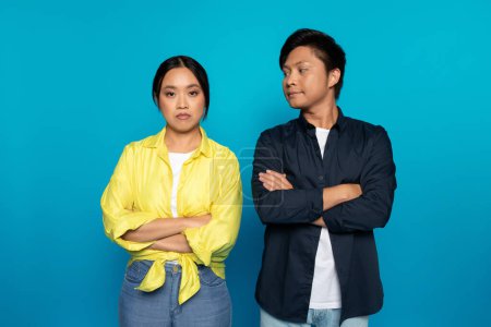 Photo for Offended sad bored millennial asian lady ignoring husband in casual crossed arms on chest, after quarrel, isolated on blue studio background. Emotions, relationship problems, bad mood, pms - Royalty Free Image