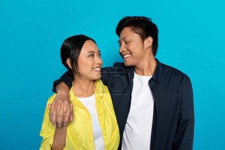Photo for Cheerful millennial asian couple in casual hugs, enjoy date at spare time together, isolated on blue studio background. Emotions romantic, ad and offer, relationships and love - Royalty Free Image