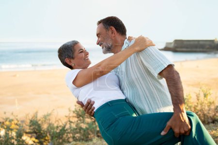 Photo for Oceanside Vacation Romance. Mature husband and wife hugs engaging in a spontaneous dance during their seaside getaway with view on beach and waves at summer sunset - Royalty Free Image