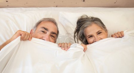 Téléchargez les photos : Souriant vieux caucasien homme et dame se réveille au lit, profiter de bonne matinée ensemble, s'amuser sous couverture dans la chambre, vue sur le dessus. Week-end et temps libre, relation et amour, mode de vie, détente - en image libre de droit