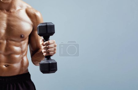 Photo for Unrecognizable muscular athlete guy with perfect abs holding dumbbell flexing arm muscles over gray background. Strength bodybuilding workout. Cropped shot, Empty space for text - Royalty Free Image