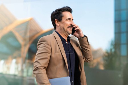 Téléchargez les photos : Portrait d'un homme d'affaires d'âge moyen joyeux parlant au téléphone avec un partenaire d'affaires ou un client tout en restant debout à l'extérieur, regardant l'espace de copie. Entrepreneuriat, concept de communication - en image libre de droit