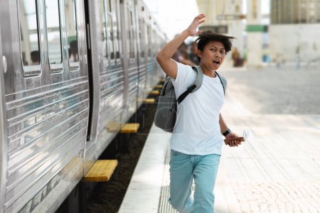 Photo for Stressed young asian man student with backpack tourist running by train station platform, chinese guy chasing departing train. Traveler late on plane trip - Royalty Free Image
