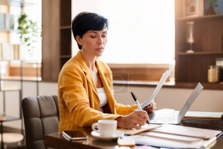 Photo for Serious Middle Aged Business Woman Taking Notes Near Laptop Computer, Writing Report Working With Papers Sitting At Desk In Modern Office Workplace. Entrepreneurship Career Concept - Royalty Free Image