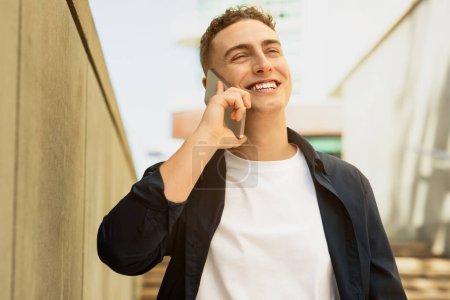 Photo for Cheerful millennial european man enjoy lifestyle, calling by smartphone, got good news in city, free space, close up. Work, success business, study and conversation, communication - Royalty Free Image