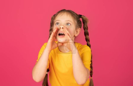 Photo for Cute little girl keeping hands near mouth and shouting at copy space, preteen female child making announcement, sharing news while standing isolated over pink studio background, copy space - Royalty Free Image