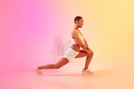 Photo for Focused active slim millennial latin woman athlete in sportswear doing lunges for legs on neon pink studio background, profile. Workout, fitness and sport, body care exercises - Royalty Free Image