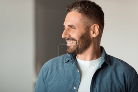 Photo for Cheerful middle aged man with stubble smiling while looking aside indoor, portrait shot of charismatic european guy expressing positivity and success. Side view shot - Royalty Free Image