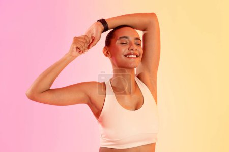 Téléchargez les photos : Glad mince jeune athlète dame latine en vêtements de sport profiter de l'entraînement, étirant les mains sur fond de studio rose fluo. Sports, soins du corps et bien-être, soins de santé, perte de poids et remise en forme - en image libre de droit
