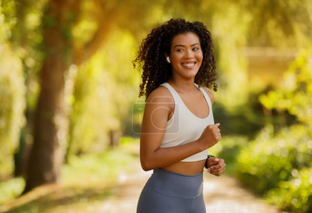 Photo for Athletic brazilian lady in sportswear exercising in sunny park, wearing wireless earbuds and listening to playlist during morning workout. Healthy lifestyle and motivation - Royalty Free Image