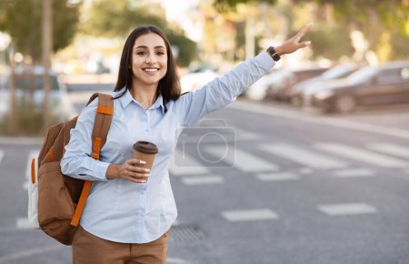Téléchargez les photos : Jolie jeune femme européenne souriante avec sac à dos, tasse de café à emporter, arrêt de taxi avec pancarte à la main en ville à l'extérieur. Dame profiter du voyage, Voyage touristique, annonce et offre, style de vie - en image libre de droit