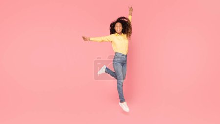 Téléchargez les photos : Femme noire gracieuse posant et sautant, mettant en valeur son style sur fond rose vif, pleine longueur, panorama avec espace libre - en image libre de droit