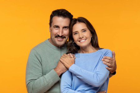 Photo for Happy senior european husband and wife in casual clothes hug and looking at camera, isolated on orange studio background. Lifestyle, relationships and love, ad and offer, close up - Royalty Free Image