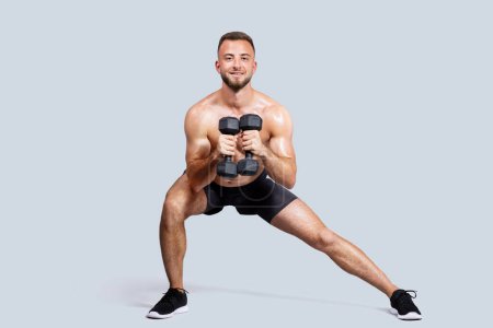 Photo for Smiling sweat strong muscular young european man with beard, naked torso make exercises with dumbbells, isolated on gray studio background. Strength workout, sport, body care - Royalty Free Image