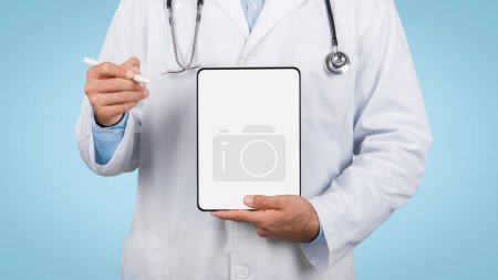 Téléchargez les photos : Professionnel médical en manteau blanc et stéthoscope, tenant une tablette numérique vierge avec stylet, prêt à prendre des notes ou à montrer des informations médicales, sur fond bleu, maquette - en image libre de droit