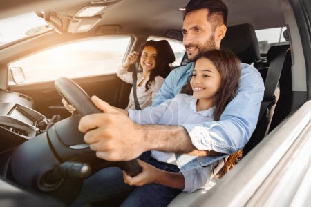 Photo for Smiling father drives with his cheerful daughter sitting beside, while mother looking at them and smiling, capturing warm family moment during a sunny day drive - Royalty Free Image