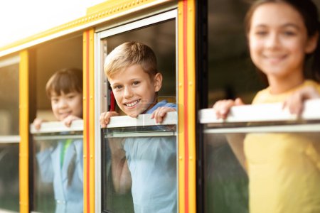 Foto de Niños felices mirando por la ventana del autobús escolar amarillo, sus caras alegres se volvieron hacia la cámara, grupo de alumnos disfrutando del viaje, listos para viajar juntos, enfoque selectivo en el niño - Imagen libre de derechos
