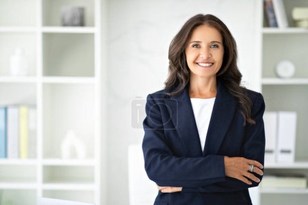 Photo for Confident attractive brunette mature woman posing in modern office, holding arms crossed on chest and smiling at camera, copy space. Career, success, business, job, occupation - Royalty Free Image