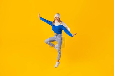 Téléchargez les photos : Femme enthousiaste en vêtements d'hiver saute joyeusement, mettant en valeur son excitation pour les ventes d'hiver sur un fond jaune vif, plan complet - en image libre de droit