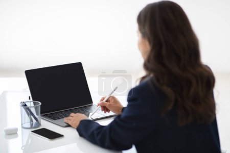 Photo for Unrecognizable woman employee using brand new laptop with empty black screen and stylus while working in office, over shoulder shot, mockup. Modern technologies - Royalty Free Image
