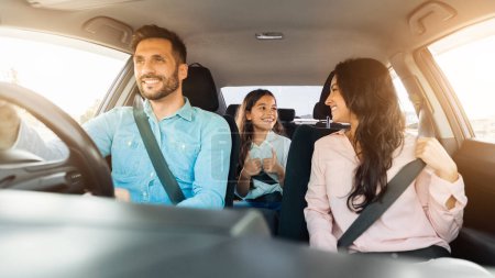 Photo for Smiling father focused on driving as his cheerful daughter in the backseat gives thumbs up, mother shares joyful moment looking towards her child - Royalty Free Image