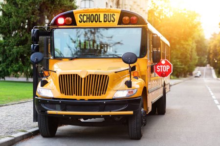 Foto de Autobús escolar amarillo anticuado con señal roja de stop en el lado estacionado en la calle calle tranquila, vehículo vacío con puertas abiertas de pie en la carretera, esperando a los estudiantes, listo para recoger a los niños - Imagen libre de derechos