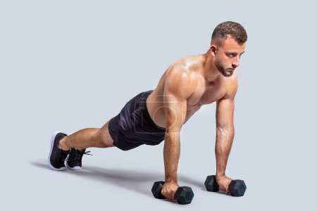 Photo for Focused strong muscular young european man make exercises with dumbbells for hands, push ups, isolated on gray studio background. Strength training, body care and power, full length - Royalty Free Image