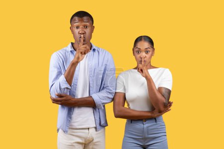 Photo for Both african american man and woman pose with fingers to their lips in hush gesture, signaling secrecy or the need for quiet, yellow background - Royalty Free Image