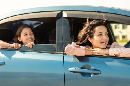 Téléchargez les photos : Mère joyeuse et sa fille partagent un moment spécial, tous deux penchés par la fenêtre de la voiture, se prélasser dans la lumière du soleil et sentir le vent, reflétant le bonheur pur et collant - en image libre de droit