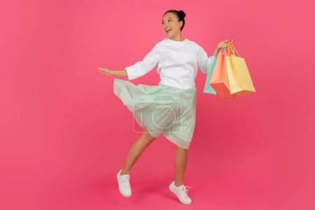 Téléchargez les photos : Big Sales Concept. Jeune femme asiatique heureuse qui court avec des sacs à provisions colorés sur fond rose, Lady Shopaholic coréenne excitée bénéficiant de réductions saisonnières, Prise de vue pleine longueur, Espace de copie - en image libre de droit