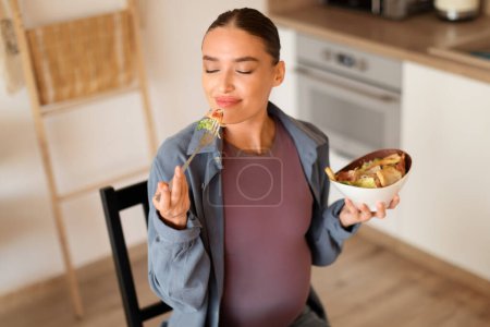 Foto de Mujer embarazada deliciosamente sabores forkful de ensalada de su tazón, apreciando los sabores y nutrientes beneficiosos para su viaje de embarazo - Imagen libre de derechos