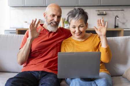 Photo for Happy Senior Couple Making Video Call With Laptop At Home, Cheerful Elderly Spouses Waving Hands At Webcam While Sitting On Couch In Living Room, Enjoying Online Communication, Closeup - Royalty Free Image