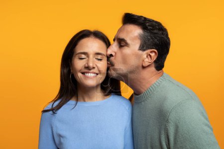 Photo for Portrait of happy old caucasian husband kiss in chick wife, enjoy free time, isolated on orange studio background. Family romantic lifestyle, relationships and love, date together, ad and offer - Royalty Free Image