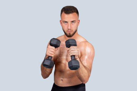 Photo for Serious sweat strong muscular young caucasian man athlete with beard, naked torso make exercises with dumbbells for hands, fights, strength workout for muscle biceps, isolated on gray background - Royalty Free Image