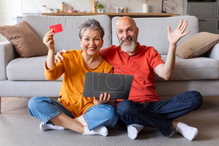 Photo for Easy Payments. Portrait Of Senior Couple With Laptop And Credit Card Sitting On Floor At Home, Happy Cheerful Elderly Spouses Enjoying E-Commerce, Paying Bills Online And Smiling At Camera - Royalty Free Image