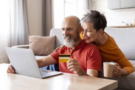 Photo for Smiling mature family couple holding bank credit card and looking at laptop screen, elderly spouses entering payment information, enjoying fast money transfer service or online shopping at home - Royalty Free Image