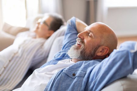 Photo for Happy Relaxed Senior Spouses Leaning Back On Comfortable Couch, Smiling Man And Woman Resting With Hands Behind Head, Relaxing On Sofa In Living Room, Side View Shot With Selective Focus - Royalty Free Image
