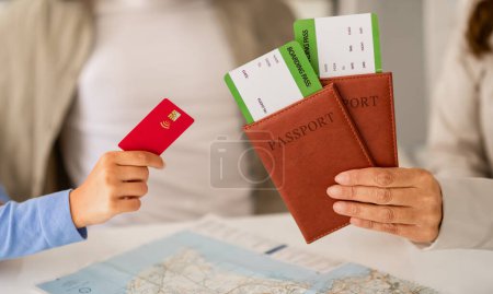 Photo for Cropped of couple meeting with a travel agent or visa manager. Woman agency worker sitting at her office desk with a man and woman, holding their tickets and passports, client paying with credit card - Royalty Free Image