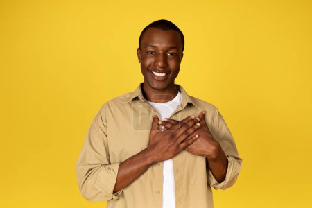 Photo for Glad handsome young black man presses hands to chest, enjoy good news, isolated on yellow studio background. Thanks gesture, gratitude sign, love people emotions and lifestyle - Royalty Free Image