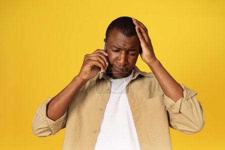 Photo for Sad millennial black guy in casual call on phone, talk, suffer from mistake, isolated on yellow studio background. Problems at communication, remotely app, bad news, stress - Royalty Free Image