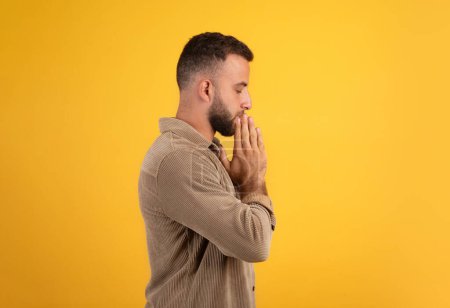 Photo for Serious calm millennial european guy make pray gesture, make a wish, isolated on orange background, studio, profile. Lifestyle, dream come true and hope, faith and belief - Royalty Free Image