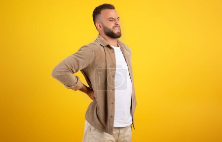 Foto de Triste infeliz hombre europeo milenario con barba en retención casual con las manos, sufren de dolor, aislado en el fondo del estudio naranja. Personas emociones, problemas de salud - Imagen libre de derechos