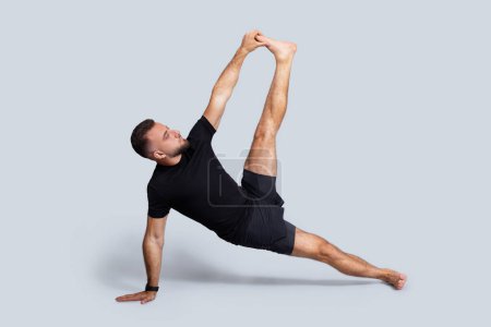 Photo for Serious millennial caucasian man in sportswear practice yoga, stretching leg, breath exercises, enjoy sport, isolated on gray studio background. Health and body care, lifestyle and vitality - Royalty Free Image
