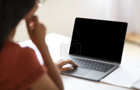 Téléchargez les photos : Sur l'épaule prise de vue d'une femme d'affaires méconnaissable travaillant sur un ordinateur portable avec écran noir vide, les mains tapant sur le clavier de l'ordinateur tout en travaillant au bureau, image recadrée - en image libre de droit