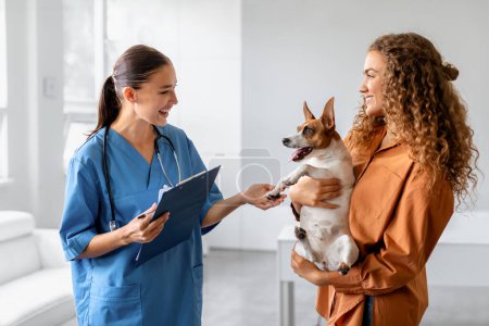 Hund, der von seiner Besitzerin während der tierärztlichen Beratung gehalten wird, mit freundlichem Tierarzt, der Notizen macht, die einen positiven Tierarztbesuch und die Interaktion mit dem Haustier veranschaulichen