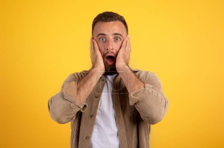 Photo for Scared shocked young european man with beard in casual with open mouth put hands to face, isolated on yellow studio background. Surprise reaction, human emotions and news - Royalty Free Image