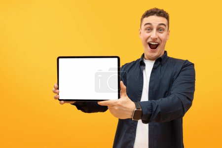 Photo for Excited emotional handsome young guy showing digital tablet with white empty screen mockup, isolated on yellow studio background, copy space for advertisement. Great deal, nice app - Royalty Free Image