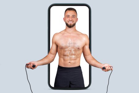 Photo for Happy sweat strong muscular young european man with beard, naked torso make exercises with skipping rope on phone screen, isolated on gray studio background. Sport app, cardio workout, blog - Royalty Free Image
