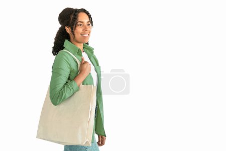 Foto de La sonriente dama afroamericana sostiene la bolsa de compras de lino orgánico posando sobre un fondo blanco, simbolizando el compromiso con las compras ecológicas y sin estilo de vida plástico. Copiar espacio - Imagen libre de derechos