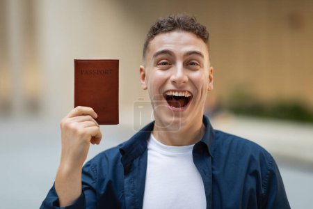Photo for Portrait of glad excited attractive millennial caucasian guy student in casual with open mouth show passport in city gray wall, outdoor, close up. People emotions, study, ad and offer - Royalty Free Image